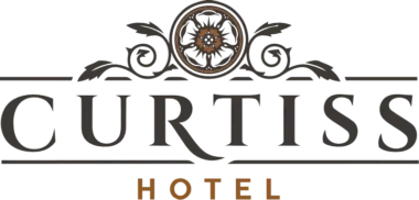A logo for curtiss hotel featuring elegant script lettering in a dark green and orange color scheme, with ornate floral and scroll decorations above and around the text.